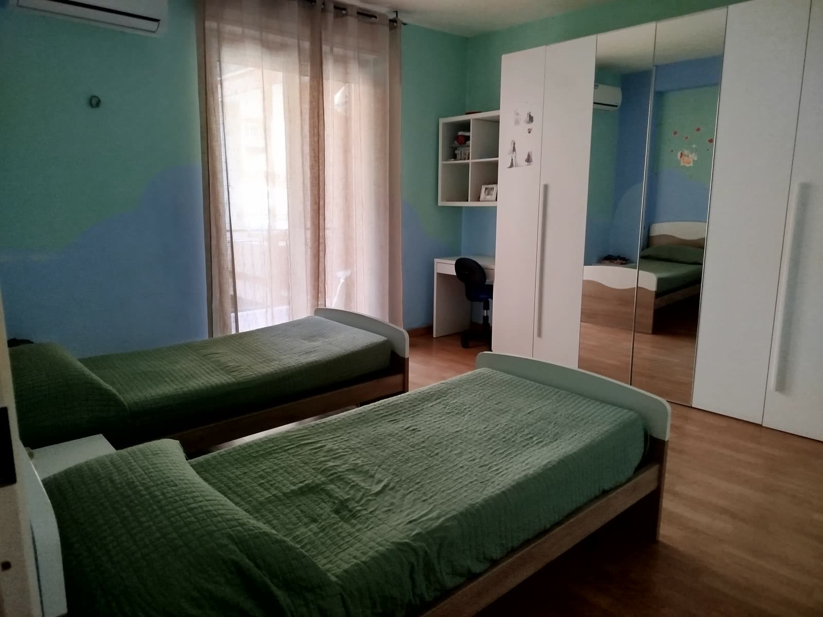 Camera con letti singoli verdi e armadio a specchi nella comunità Costruttivamente